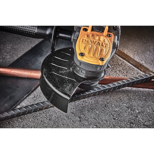 Close-up view of a DEWALT power tool, specifically an angle grinder, cutting through a metal rod on a rough concrete surface.