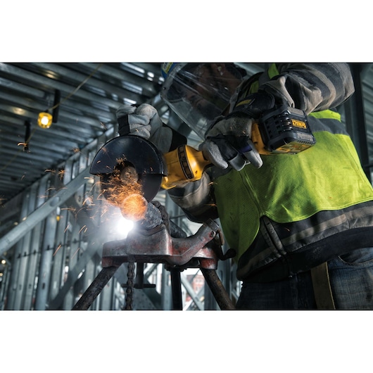 A worker wearing safety gear uses a DEWALT cordless angle grinder to cut metal, producing sparks in an industrial setting.