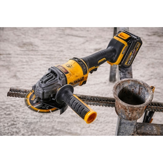 Photo of DEWALT DCG414T2 cordless grinder cutting rebar, yellow and black, close-up view on construction site.