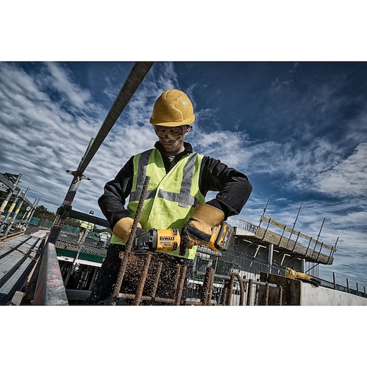 Worker uses DEWALT tools DCZ507T2-XE, DCG418N, DCZ503X2-XE at construction site. Photography product category.