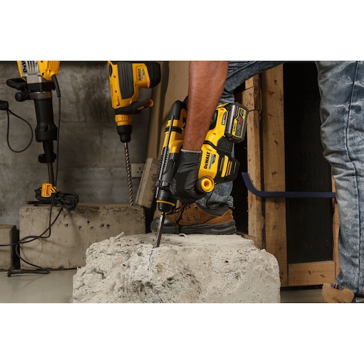 Person using a DEWALT DCH333NT cordless rotary hammer on a concrete block at a construction site.
