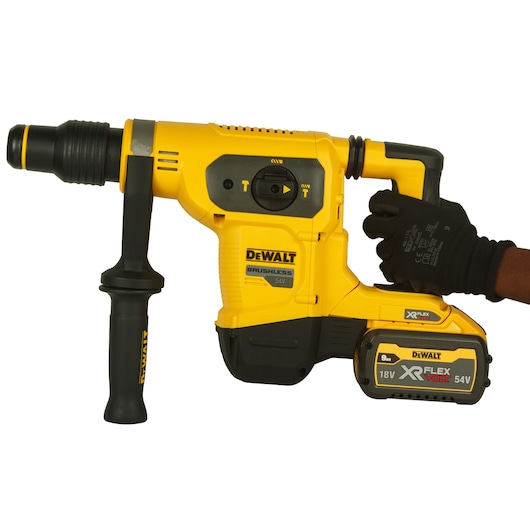 A close-up image of a DEWALT-branded yellow and black cordless power tool, specifically a rotary hammer drill, with a handle and battery pack. The tool is being held by a person wearing a black glove.