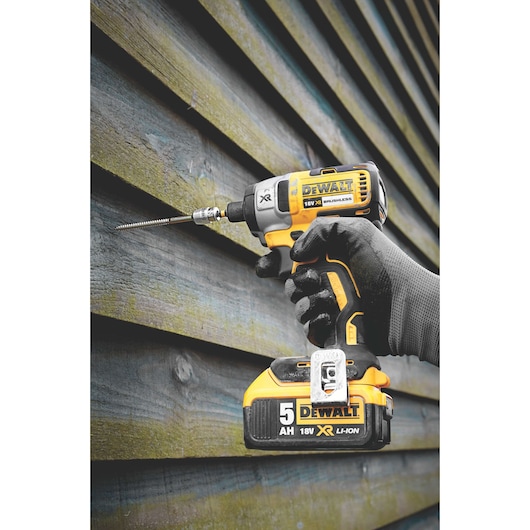 A gloved hand holding a DEWALT 18V XR Li-Ion cordless impact driver with a drill bit, working on wooden paneling.