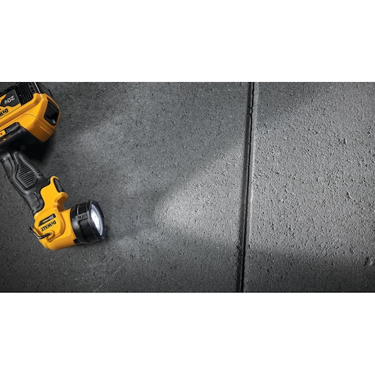 A yellow and black DEWALT handheld flashlight (model DCL040) shines light onto a rough concrete surface. The flashlight is battery powered and partially shown on the left side of the image.