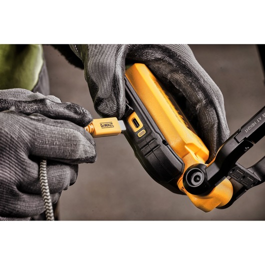 Close-up of a person wearing work gloves plugging a DEWALT USB cable into a yellow DEWALT device, likely a portable light.
