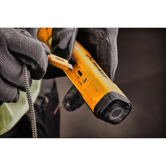A close-up view of gloved hands connecting a charging cable to a yellow DEWALT handheld device, likely related to photography or inspection.