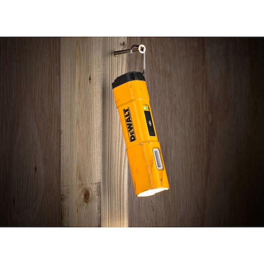A yellow DEWALT portable LED work light (model DCL183-KR) is hanging from a screw on a wooden wall, illuminating downward.
