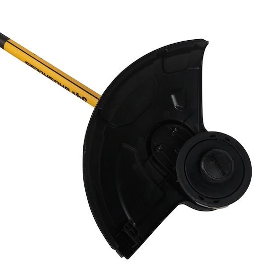 Close-up of the cutting head and protective guard of a DEWALT DCM571N brushless grass trimmer, showing the black and yellow shaft and trimmer spool.