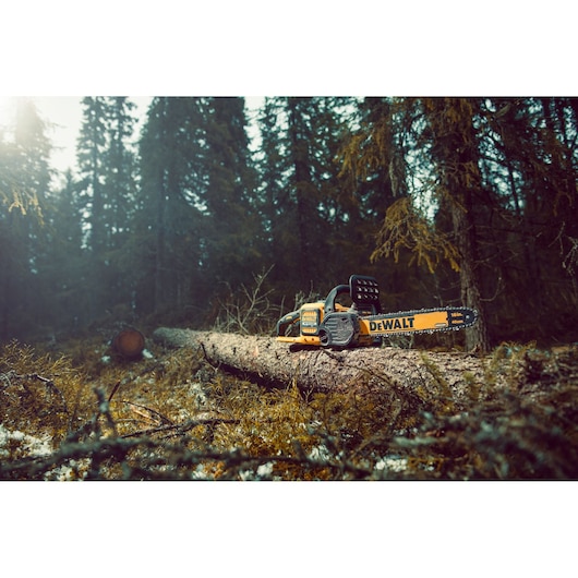 DEWALT chainsaw DCM575N on a fallen tree in a forest; tool is ready for outdoor wood cutting.