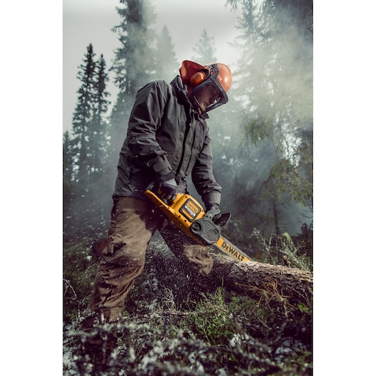Person using a DEWALT DCM575N chainsaw to cut a log outdoors, wearing protective gear in a forest setting.