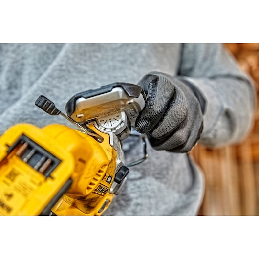 Close-up of a person wearing black work gloves adjusting the settings on a yellow DEWALT cordless jigsaw tool.