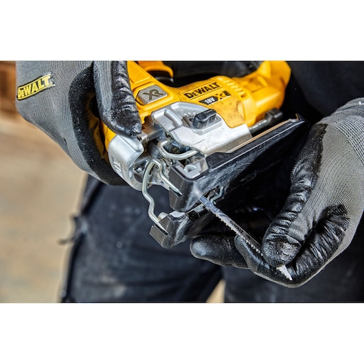 Close-up of a person wearing gloves handling a DEWALT 18V XR cordless jigsaw, preparing to insert or remove the saw blade.