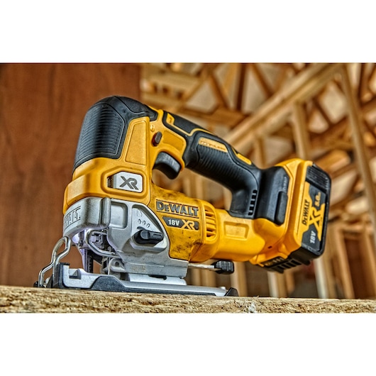 A close-up of a DEWALT 18V XR cordless jigsaw placed on a wooden surface at a construction site.