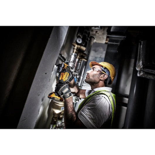 Worker using DEWALT DCS355D2 cordless tool on wall, wearing hard hat and gloves in an industrial setting.