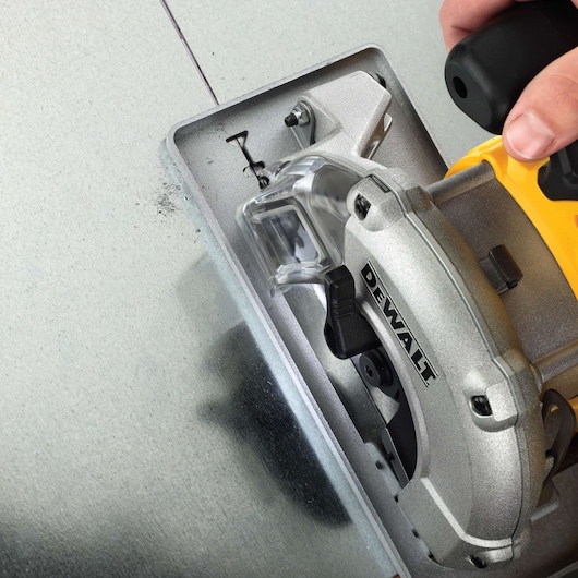 Close-up of a DEWALT circular saw cutting through a sheet of metal, showing the blade and protective guard.