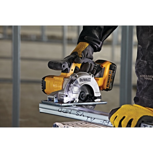 DEWALT cordless metal cutting saw in use, worker wearing gloves and safety gear, cutting steel profile indoors.