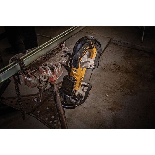 A DEWALT cordless band saw is shown cutting a metal pipe held in a clamp in a workshop setting.