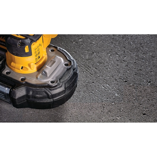 Close-up view of the base of a yellow and black DEWALT power tool resting on a textured concrete surface.