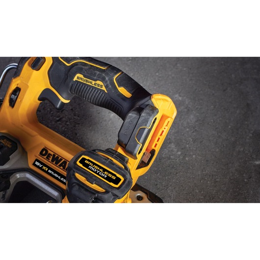Close-up view of a DEWALT cordless power tool with yellow and black brushless motor details, showing part of the handle and battery pack against a dark surface.