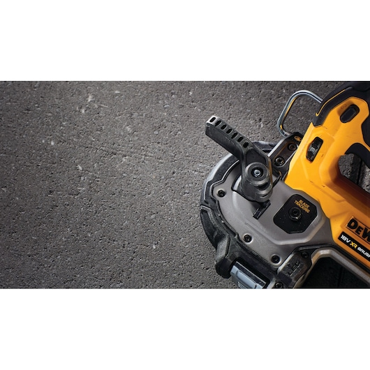 Close-up view of a DEWALT power tool, partially visible, showing its cutting blade and adjustment handle on a rough, gray concrete surface.