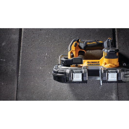 A yellow and black DEWALT cordless band saw, model DCS377NT, is shown placed on a concrete surface. The tool features a compact design and ergonomic handle.