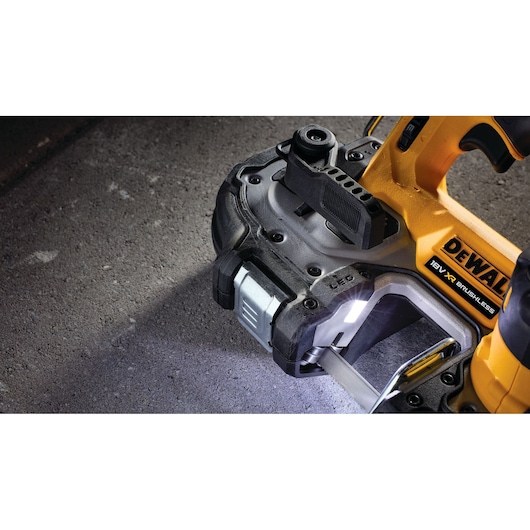Close-up of a DEWALT 18V XR brushless portable band saw cutting a metal object, with LED work light illuminated, on a concrete surface.