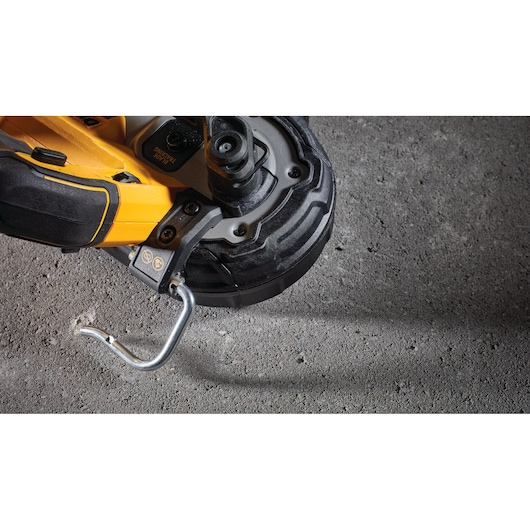Close-up view of a DEWALT power tool positioned on a rough concrete surface, focusing on the tool's yellow and black body and metal hook attachment.