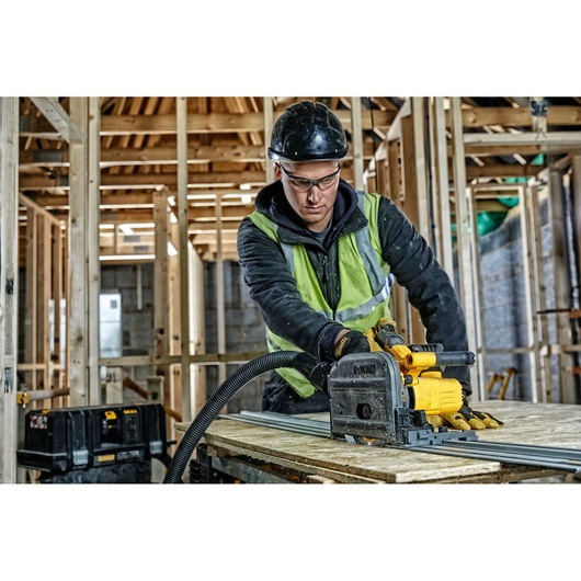 Worker uses a DEWALT DCS520NT saw to cut wood at a construction site with timber framing visible.
