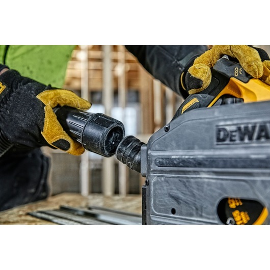 Close-up of gloved hands connecting a hose to a DEWALT power tool at a construction site.