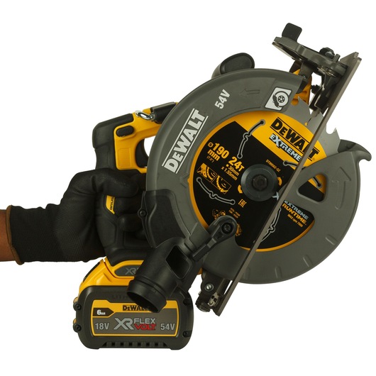 A close-up image of a person wearing a black glove holding a DEWALT cordless circular saw. The saw features a yellow and gray design, DEWALT branding, and an XR FLEXVOLT 18V/54V lithium-ion battery attached.