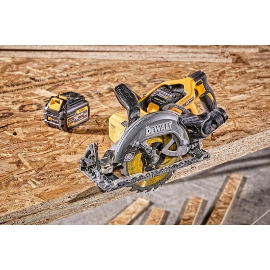 A DEWALT cordless circular saw placed on a wooden board, with a DEWALT XR Lithium-Ion battery visible nearby. The tools are set in a workshop environment.