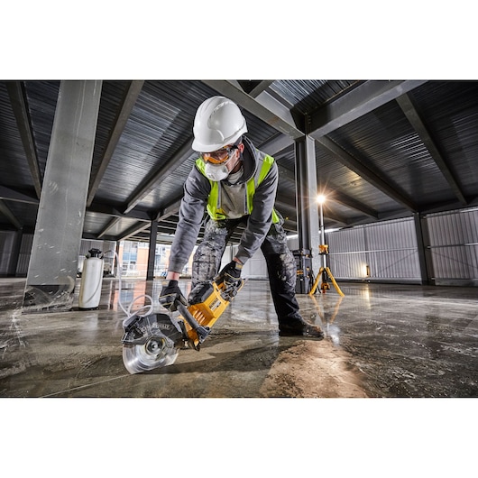 Worker with safety gear uses a DEWALT DCS690N power saw to cut concrete on a construction site indoors.