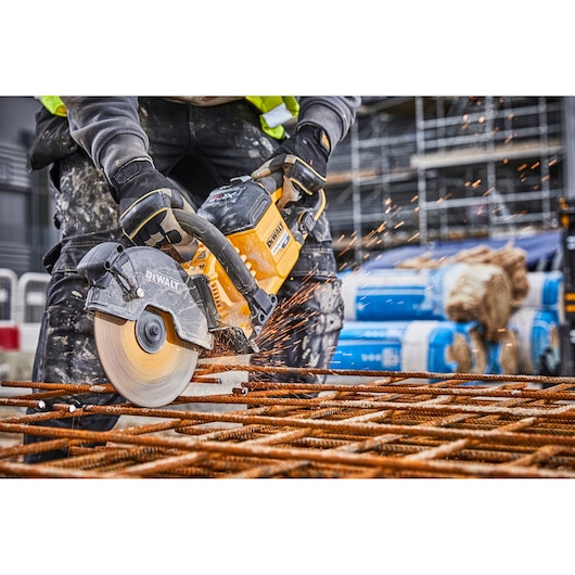 Worker uses DEWALT DCS690N saw to cut metal rods, sparks flying, at a construction site.