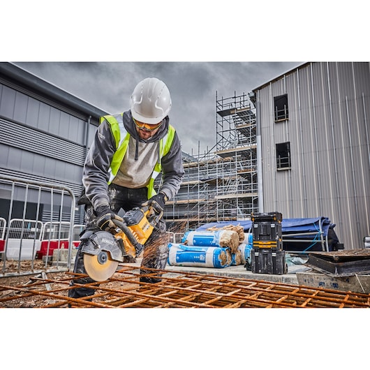 Worker using a DEWALT DCS690N saw to cut metal rods on a construction site with safety gear and equipment.