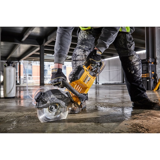 Worker using a DEWALT DCS690N saw to cut concrete floor at construction site, wearing gloves and protective clothing.