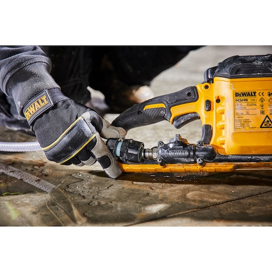 Gloved hand connects hose to a yellow DEWALT DCS690 power tool placed on a wet concrete surface.