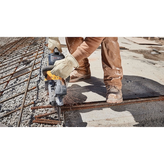 Worker cuts metal rebar with a DEWALT saw at a construction site wearing gloves and safety boots.