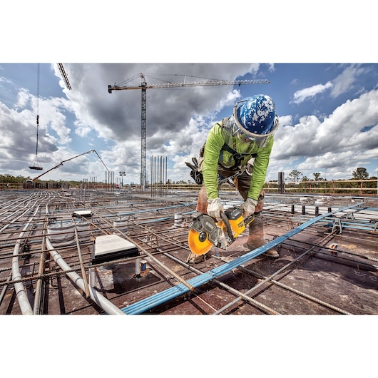 Worker using a DEWALT cut-off saw on a construction site with steel rods and cranes in the background.