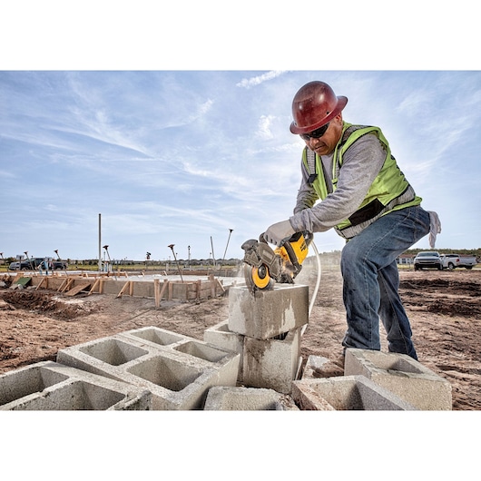 Worker uses DEWALT cutting tool on concrete blocks at construction site. Wearing safety gear.