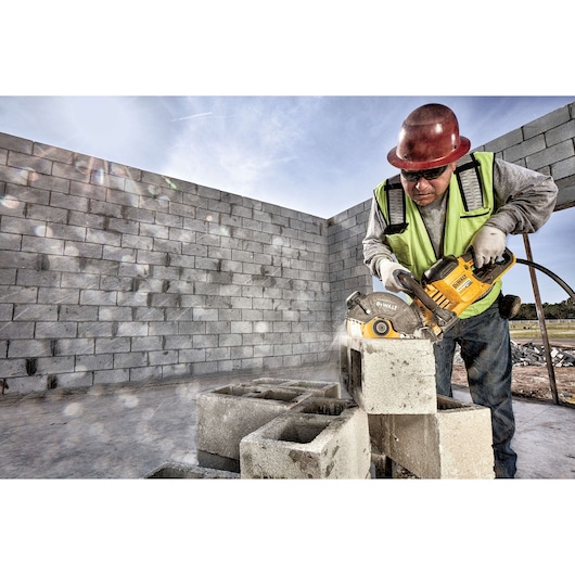 Worker using DEWALT saw to cut concrete blocks at a construction site, wearing safety gear and helmet.