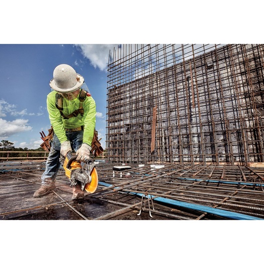 Worker using a DEWALT saw on rebar at a construction site, wearing safety gear and a hard hat.