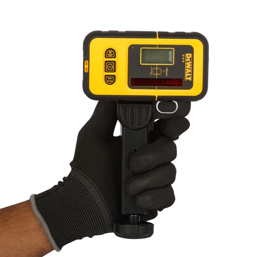 A person wearing a black glove is holding a yellow and black DEWALT laser detector, model DE0892, with an LCD screen and control buttons, used for photography and construction applications.