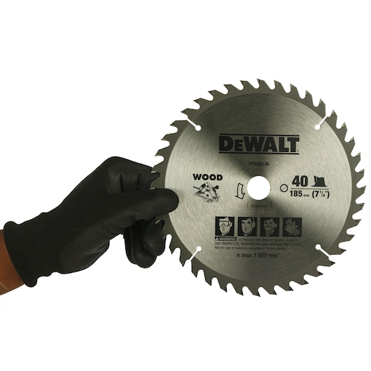 A person wearing a black glove is holding a DEWALT DT4062 circular saw blade designed for cutting wood. The blade features 40 teeth and has a diameter of 185 mm (7-1/4 inches). Safety icons and usage instructions are visible on the blade.