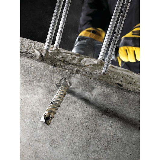DEWALT drill bit boring through concrete with steel rebars, operated by worker wearing yellow gloves.