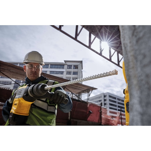 DEWALT DT60814, DT60814-QZ drill bit in use at construction site; worker with protective gear and buildings visible.