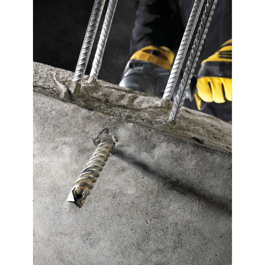 Close-up of a DEWALT drill bit boring into concrete with metal rebar and gloved hands visible.