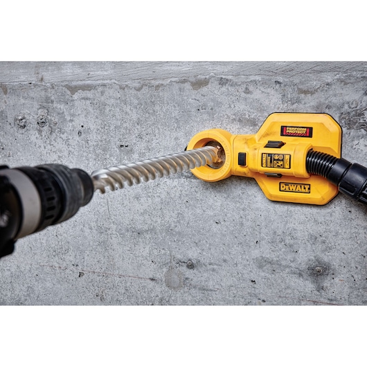 A yellow DEWALT dust extraction attachment connected to a drill, used while drilling into a concrete wall.