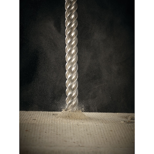 Close-up of a metallic spiral drill bit penetrating a concrete surface, releasing dust.