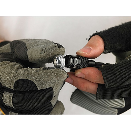A close-up of gloved hands holding a DEWALT drill bit holder, showing the textured silver collar and black body with the DEWALT logo.