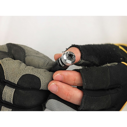 A close-up view of gloved hands holding a DEWALT screwdriver bit holder, with the bit visible at the end.